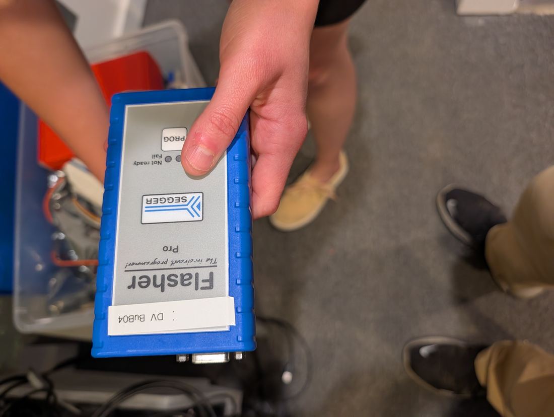 A blue SEGGER Flasher Pro held above the box of programmers and cables